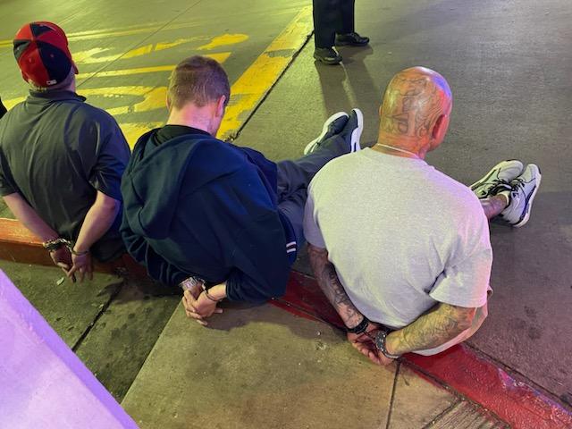 Three men in handcuffs and seated on the curb